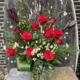 Red roses arranged in a glass vase with white filler flowers