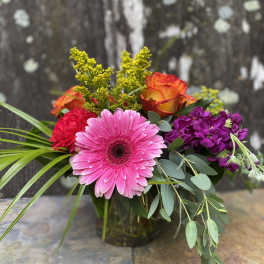Mixed bouquet with pink gerbera, orange roses, and purple flowers in a glass vase