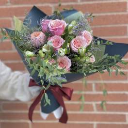 Bouquet of pink roses with purple filler and greenery wrapped in dark paper