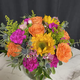 Bouquet of orange roses, yellow sunflower, and bright pink flowers in a glass vase