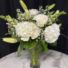 White roses and hydrangeas in a glass vase with lily buds