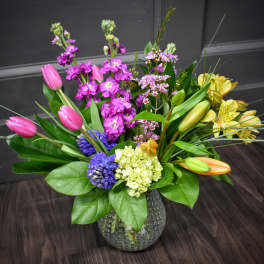 Mixed bouquet in a textured glass vase with pink tulips, purple blooms, and yellow lilies