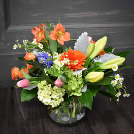 Mixed bouquet with orange blooms, lilies, and daisies in a glass vase