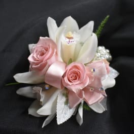 Pink roses and white lilies arranged with a pink ribbon on a dark background