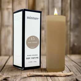 Lit beige soy votive candle beside its box