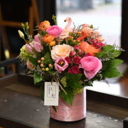 Mixed pink and orange flower arrangement with flamingo decorations in a pink vase.