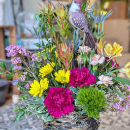 Mixed flower arrangement in a woven basket with a decorative bird