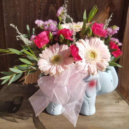 Pink and white flowers arranged in a small elephant-shaped vase with a ribbon