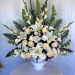 White floral arrangement in a white urn with lilies and roses