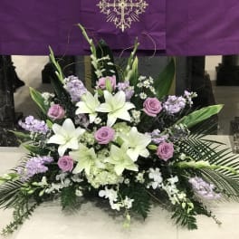 Symmetrical funeral arrangement with white lilies, lavender roses, and purple flowers
