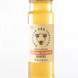 A jar of orange blossom honey with a black lid and labeled front