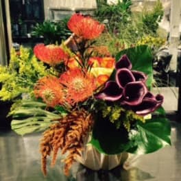 Tropical floral arrangement with orange blooms and purple calla lilies in a vase