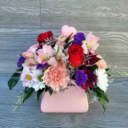 Mixed bouquet in a pink vase with red roses, pink carnations, and daisies