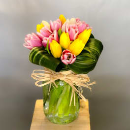 Pink and yellow tulips arranged in a glass vase with a raffia bow.