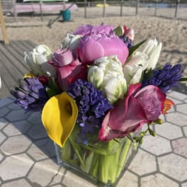 Mixed bouquet with pink roses, white tulips, purple hyacinths, and a yellow calla lily in a glass vase