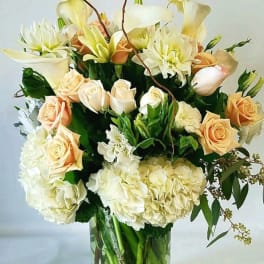 Bouquet of cream roses, white lilies, and hydrangeas in a clear glass vase