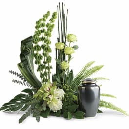 Green floral funeral urn arrangement with orchids and ferns beside a black urn