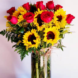 Bouquet of red roses and yellow sunflowers in a tall glass vase