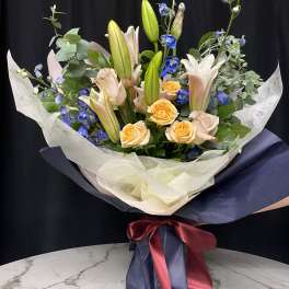 Bouquet of lilies, roses, and blue flowers wrapped in navy paper