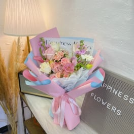 Pastel bouquet of pink, white, and lavender flowers wrapped in pink and blue paper