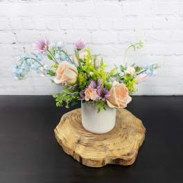 Pastel flower arrangement in a white vase on a wood slice