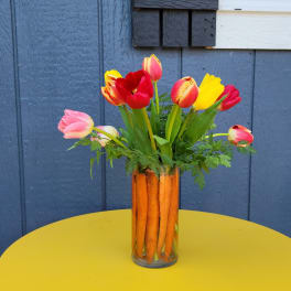 Bright tulip bouquet in a glass vase filled with upright carrots on a yellow table