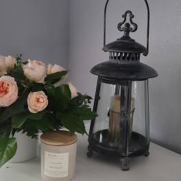 Peach roses in a white vase beside a black lantern and candle