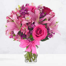 Pink and red mixed flower bouquet in a clear glass vase with a pink ribbon