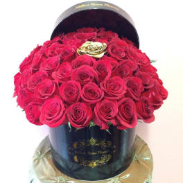Round box filled with red roses and a gold rose accent