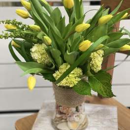 Yellow tulips and pale green hydrangeas in a glass vase wrapped with burlap