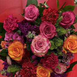Bouquet of pink, orange, and purple roses with carnations in red wrapping