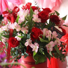 Red roses and pink lilies arranged in a red box with ribbon