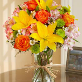 Bright mixed bouquet of yellow lilies, orange roses, and pink flowers in a glass vase