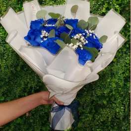 Handheld bouquet of vivid blue roses and white filler flowers wrapped in white paper