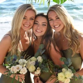 Three women holding small bouquets on a beach