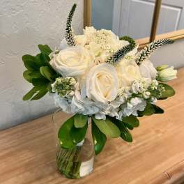 Compact white rose and hydrangea arrangement with greenery in a clear glass vase