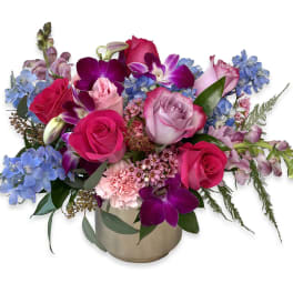 Mixed bouquet of pink roses, purple orchids, and blue flowers in a gold vase
