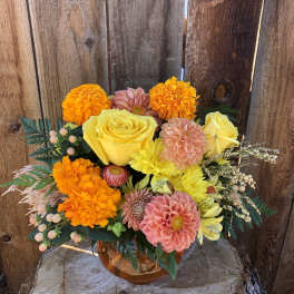 Bouquet of yellow roses, orange marigolds, and pink dahlias in an amber vase