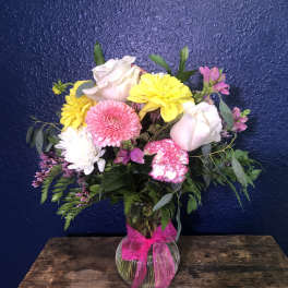Mixed pink, yellow, and white flowers in a glass vase with a pink ribbon.