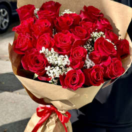 Large bouquet of red roses with white filler flowers wrapped in brown paper and a red ribbon