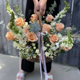 Large peach rose and white flower basket arrangement with long pastel ribbons