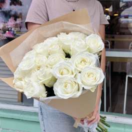 Large bouquet of white roses wrapped in kraft paper, held by a person outside a shop
