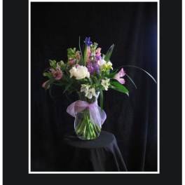 Mixed bouquet of pink, purple, and white flowers in a glass vase with a lavender bow