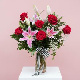 Red roses and pink lilies in a glass vase with a striped ribbon