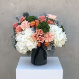 Low arrangement of white hydrangeas and peach roses in a dark ribbed vase with silver foliage