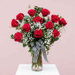 Red roses arranged in a clear glass vase with a striped ribbon