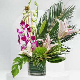 Tropical floral arrangement with orchids and lilies in a glass vase