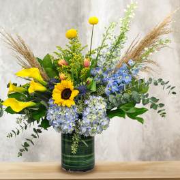 Mixed bouquet with sunflowers, calla lilies, and blue flowers in a glass vase