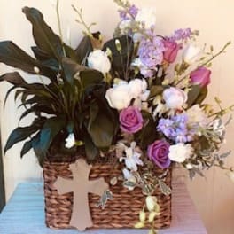 Basket arrangement of purple and white flowers with a cross decoration