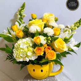 Cheerful yellow and white flower arrangement in a yellow smiley-face mug